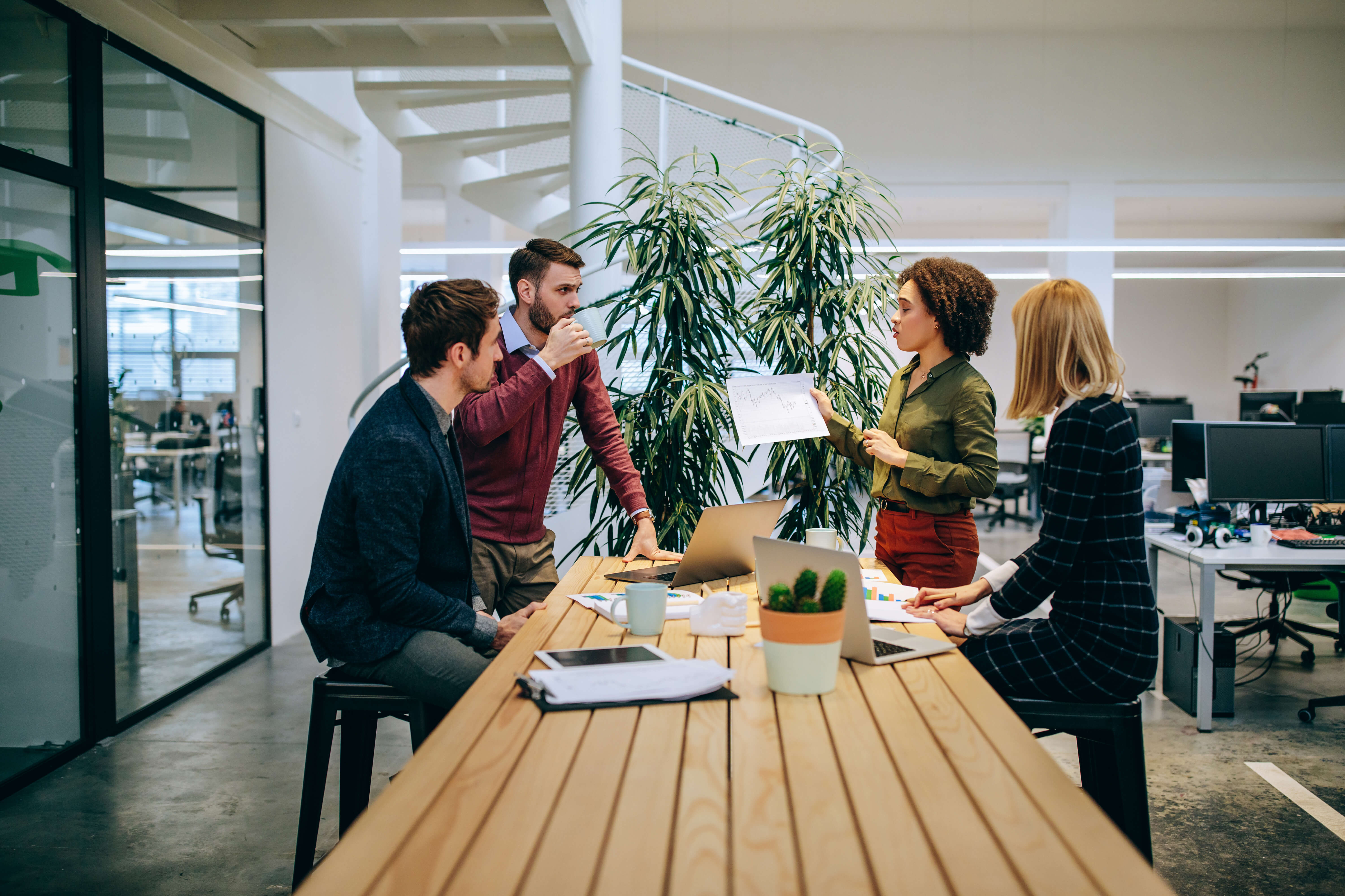 Group of please sitting and standing around a work bench in an office.